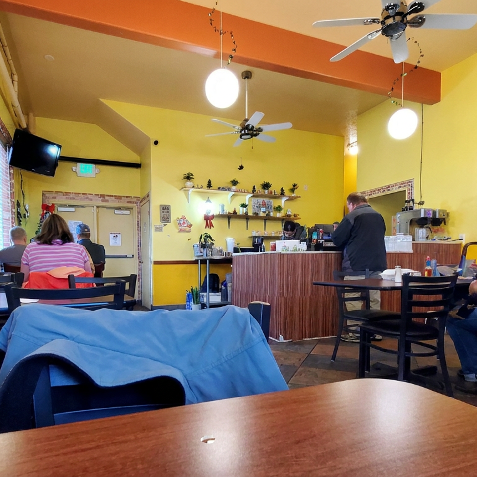 Bright yellow restaurant interior with seated diners, a counter, hanging lights, and a person holding a small dog.